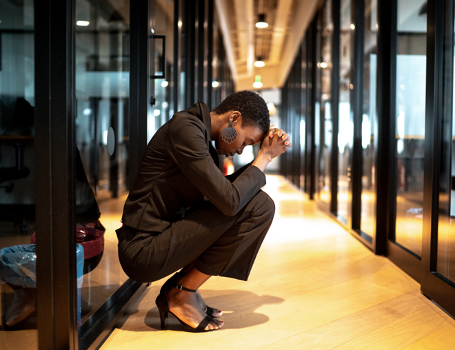 Worried person with head in hands crouched in an office hallway