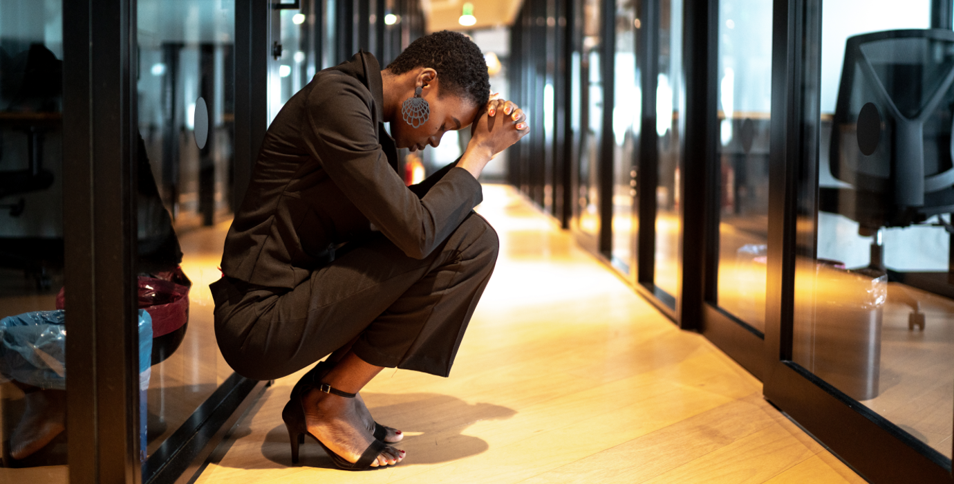 Worried person with head in hands crouched in an office hallway
