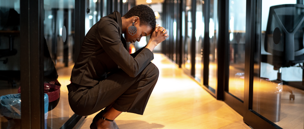Worried person with head in hands crouched in an office hallway