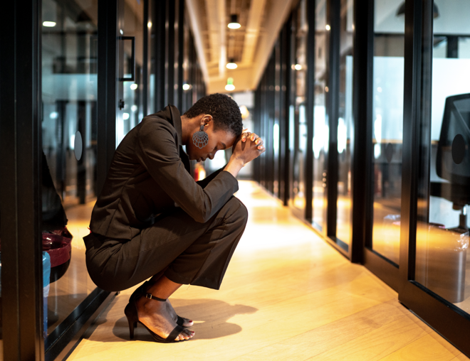 Worried person with head in hands crouched in an office hallway