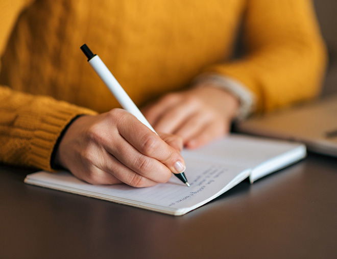 Closeup of person writing in a notebook with a pen
