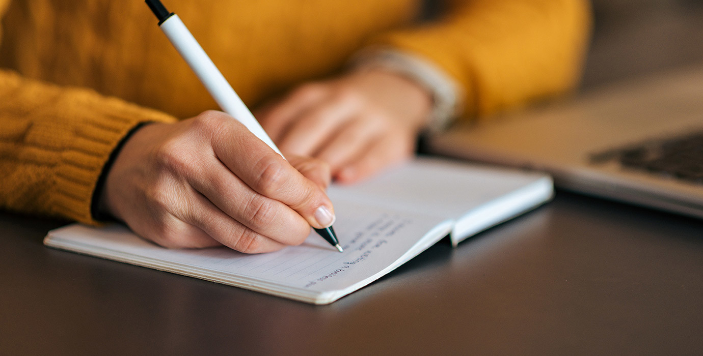 Closeup of person writing in a notebook with a pen