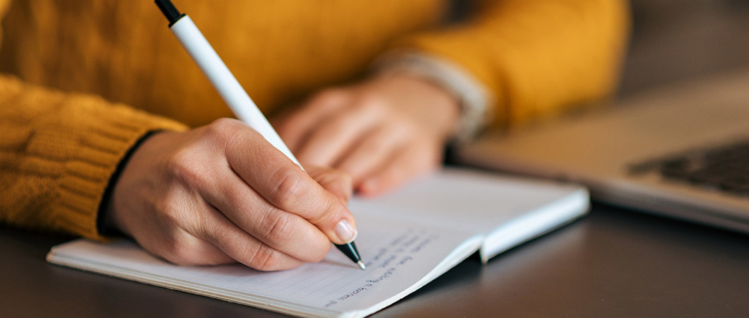 Closeup of person writing in a notebook with a pen