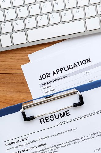 Resume, job application, notebooks, keyboard, coffee and a clock laid out on a desk