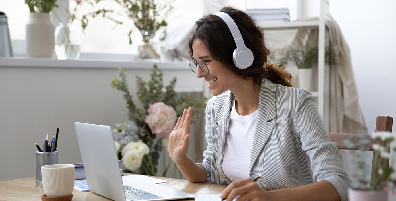 Person wearing headphones smiling and waving at a laptop