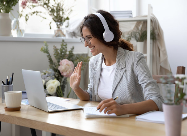 Person wearing headphones smiling and waving at a laptop
