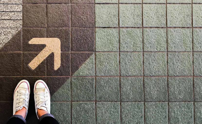 Overhead view of shoes standing on a sidewalk next to an arrow on the painted path