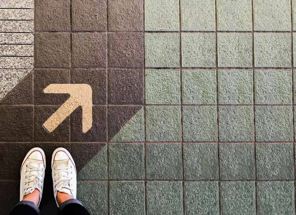 Overhead view of shoes standing on a sidewalk next to an arrow on the painted path