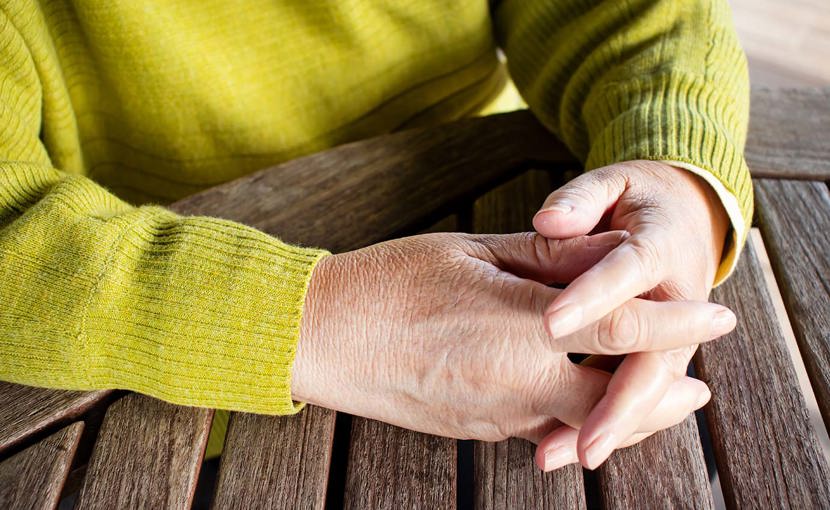 Closeup of a person's clasped hands on a wooden table