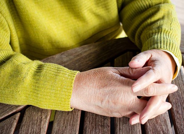 Closeup of a person's clasped hands on a wooden table