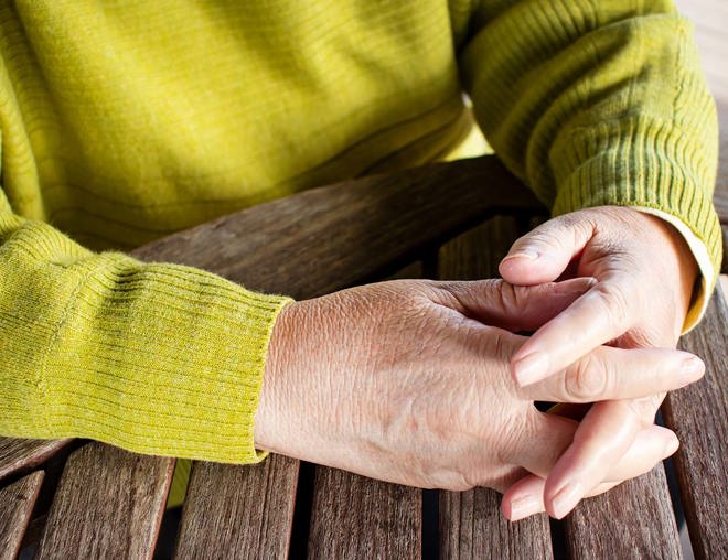 Closeup of a person's clasped hands on a wooden table