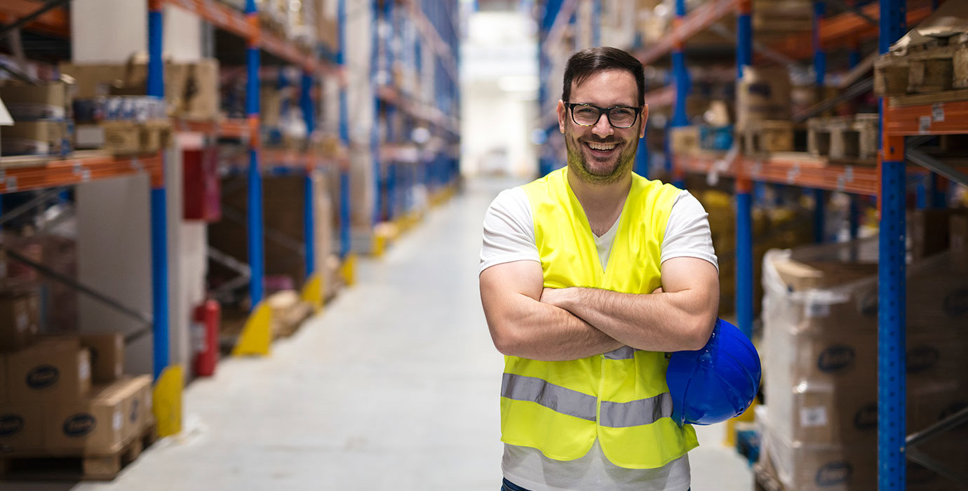 Worker wearing a safety vest smiling and standing in an aisle of a distribution centre