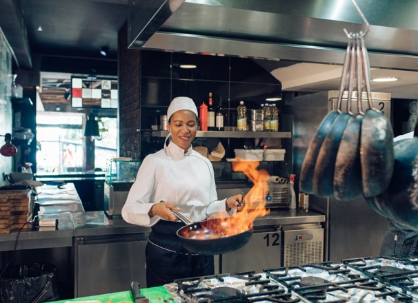 Female chef sauteing in a commercial kitchen.