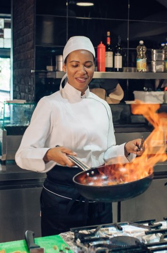Female chef sauteing in a commercial kitchen.