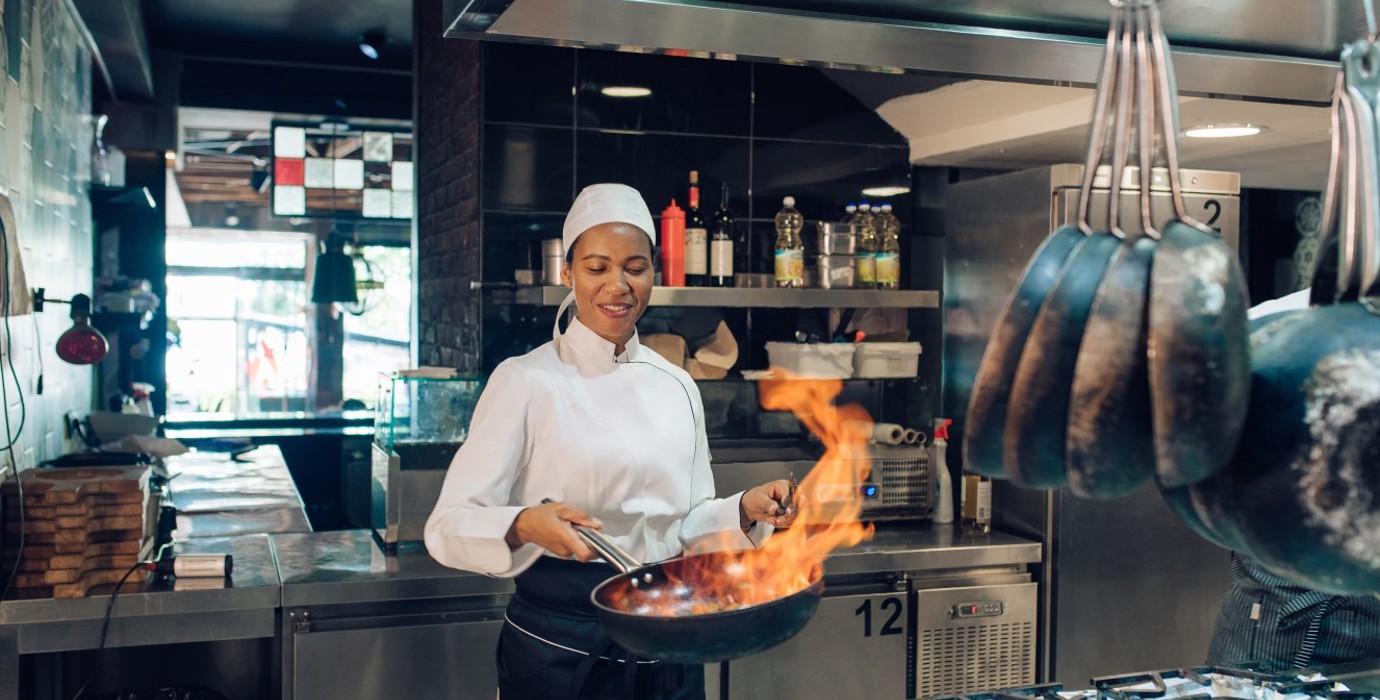 Female chef sauteing in a commercial kitchen.