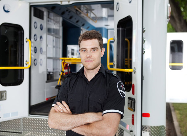 Male EMT with arms crossed standing outside of an ambulance.