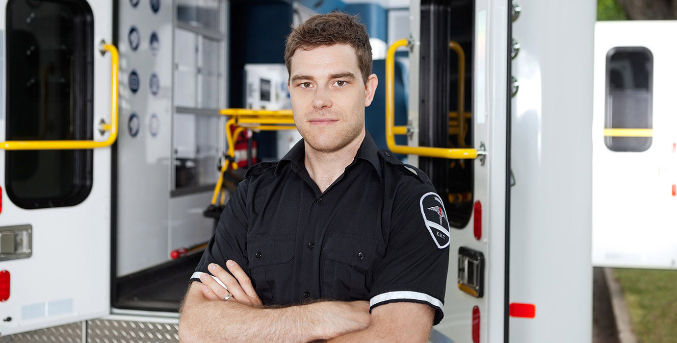 Male EMT with arms crossed standing outside of an ambulance.