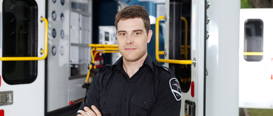 Male EMT with arms crossed standing outside of an ambulance.