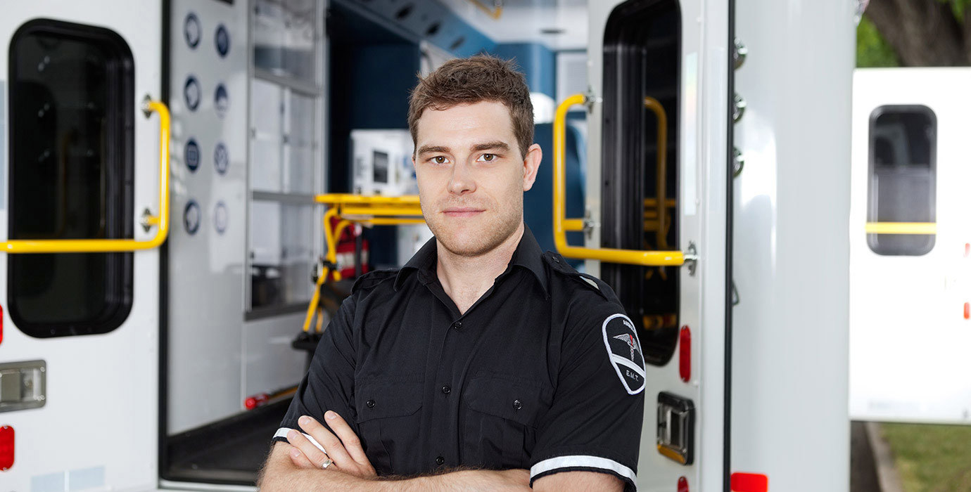 Male EMT with arms crossed standing outside of an ambulance.