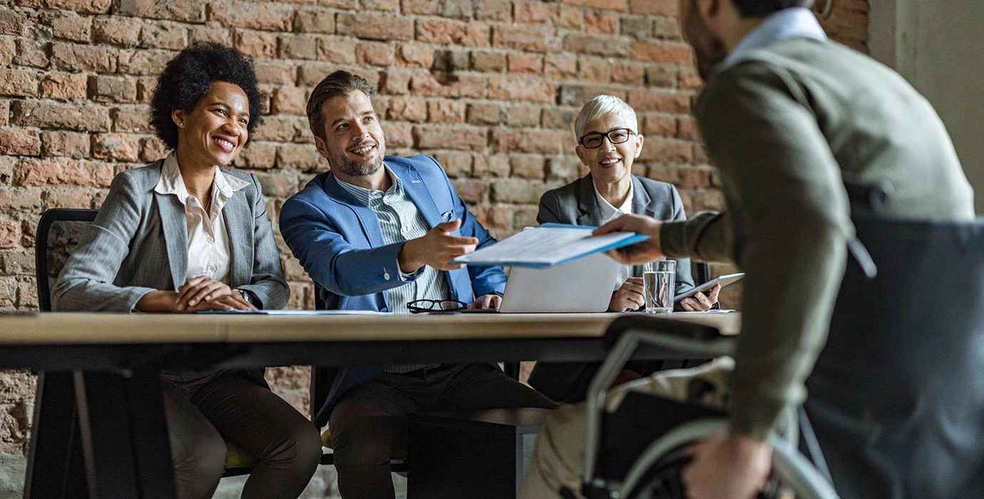 Man in wheelchair hands his resume to human resources team before a job interview.