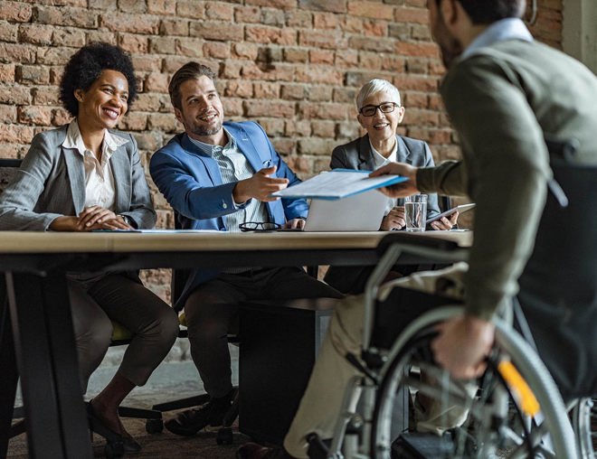 Man in wheelchair hands his resume to human resources team before a job interview.
