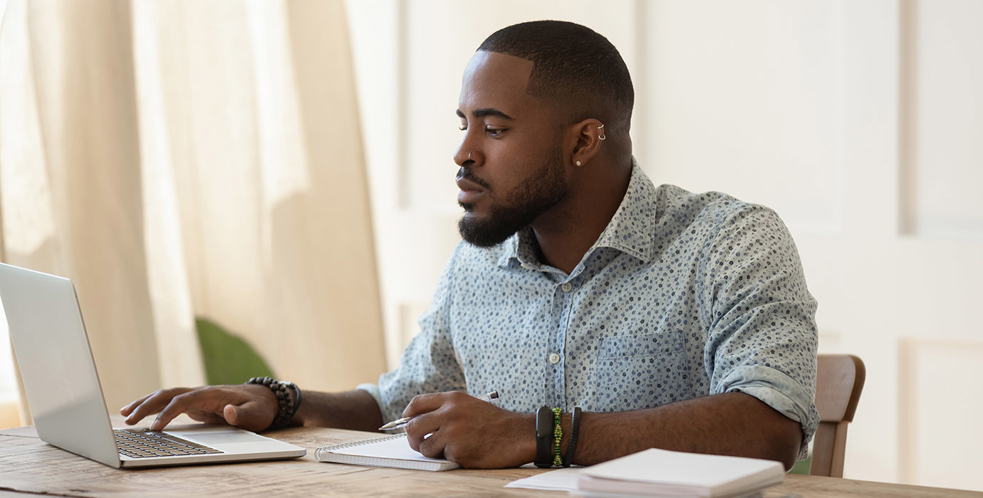 Man working on computer at desk with papers stacked beside him.