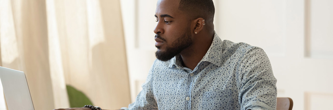 Man working on computer at desk with papers stacked beside him.