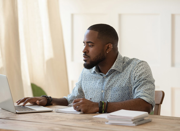 Man working on computer at desk with papers stacked beside him.