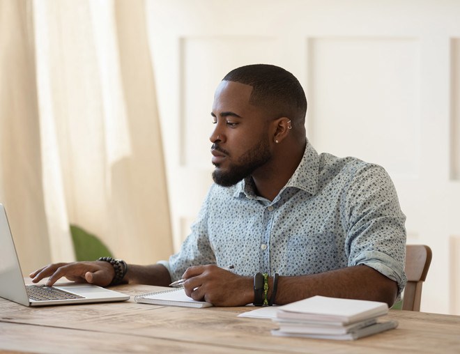 Man working on computer at desk with papers stacked beside him.