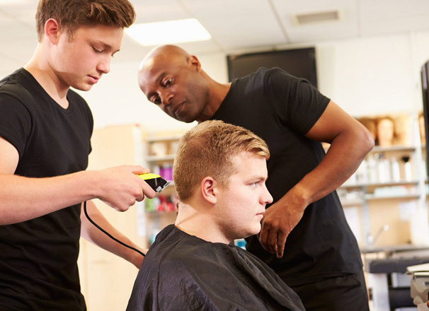 Hairdressing teacher instructs on a student on how to cut a person's hair.