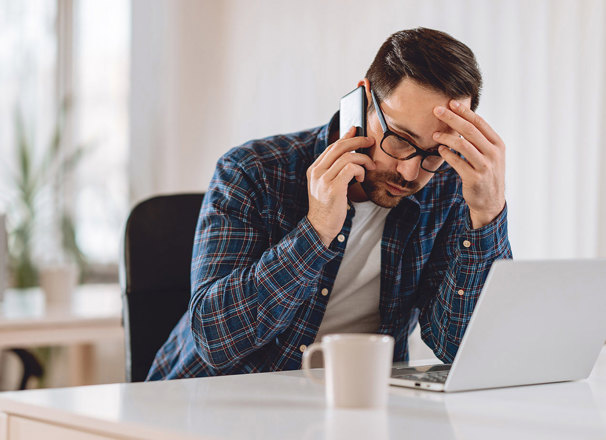 Worried man talking on phone while using laptop.