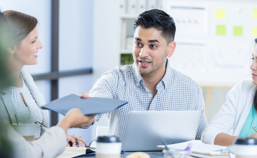 Business person passing a folder to a coworker during a meeting.