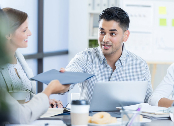 Business person passing a folder to a coworker during a meeting.