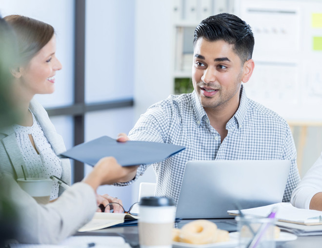Business person passing a folder to a coworker during a meeting.