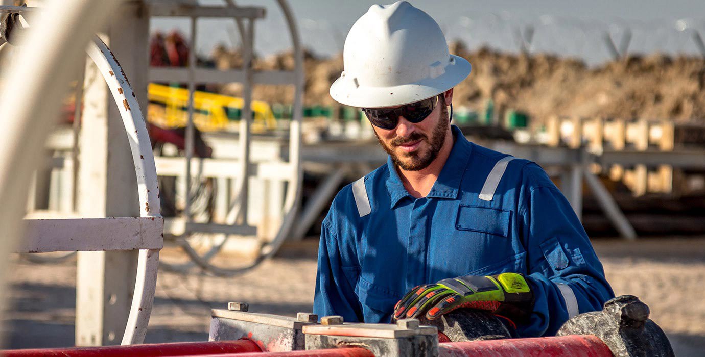 Construction worker in hard hat working on pipes outdoors.