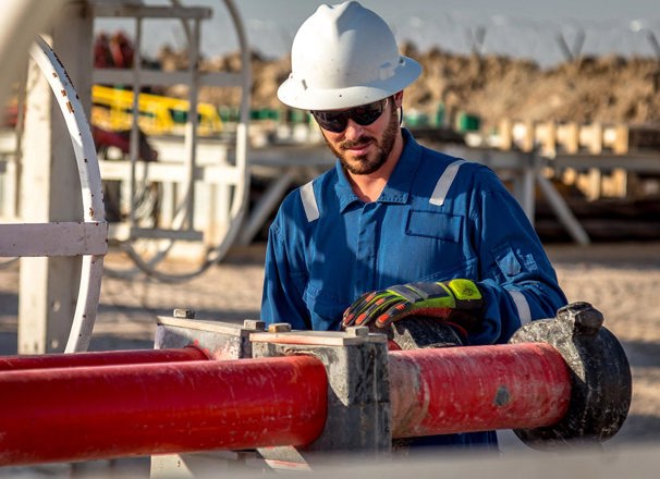 Construction worker in hard hat working on pipes outdoors.