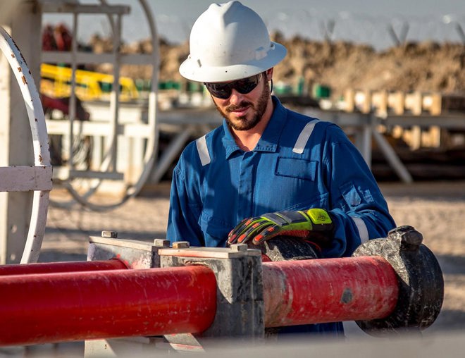 Construction worker in hard hat working on pipes outdoors.