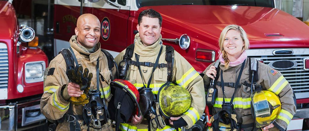 Diverse group of firefighters standing beside a firetruck.