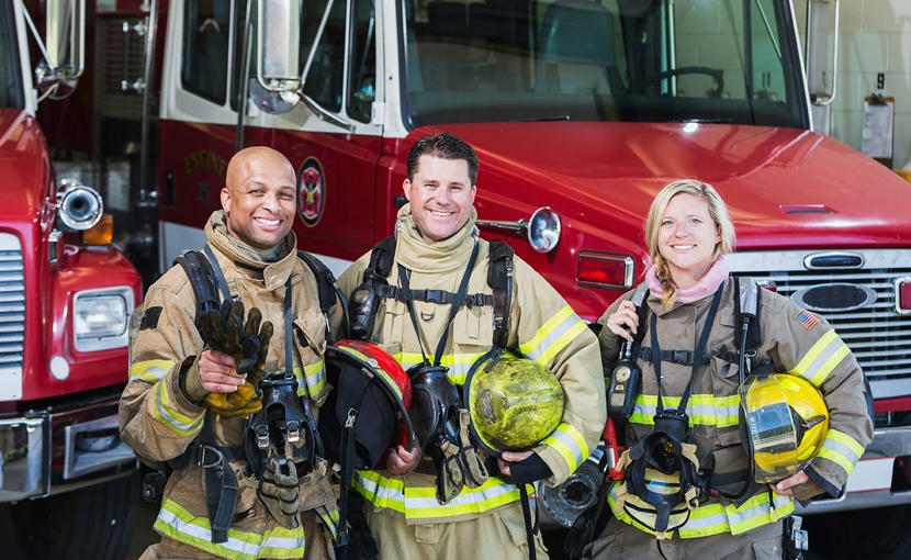 Diverse group of firefighters standing beside a firetruck.