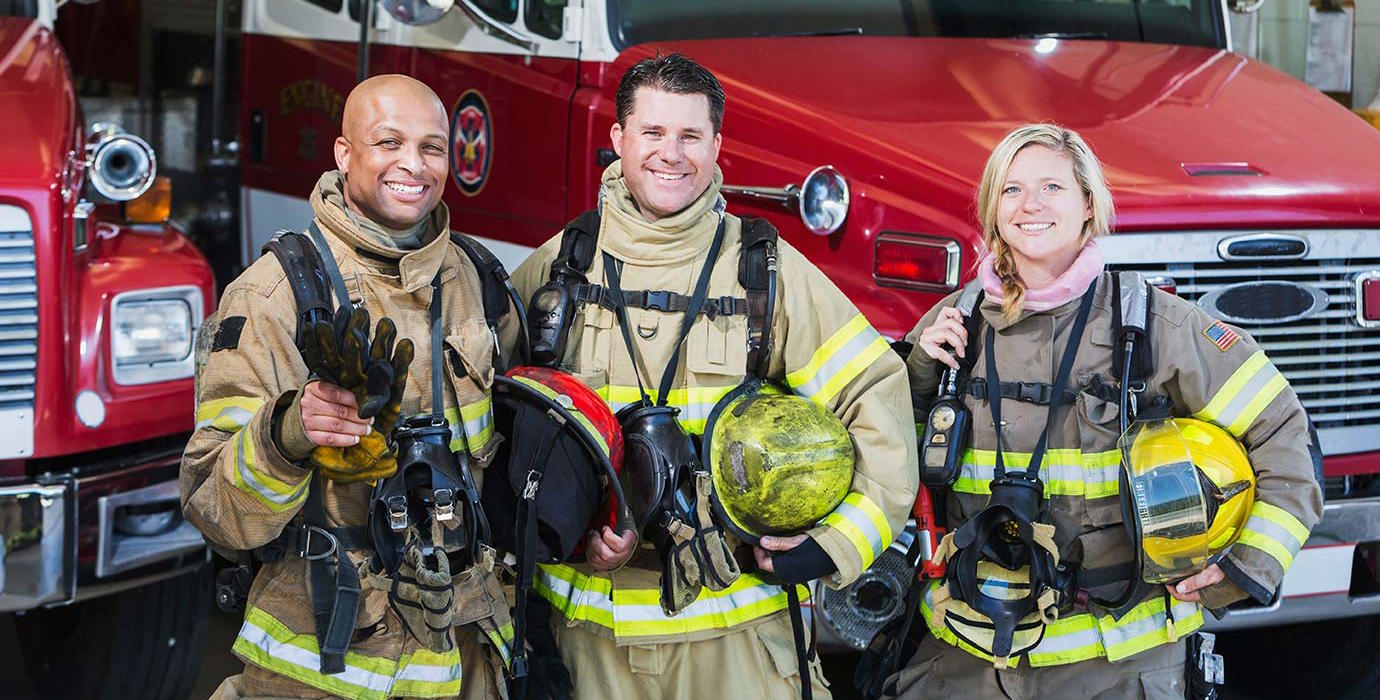 Diverse group of firefighters standing beside a firetruck.