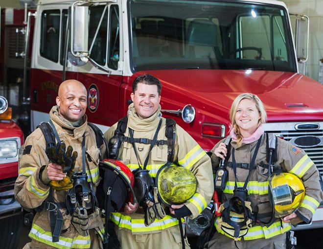Diverse group of firefighters standing beside a firetruck.