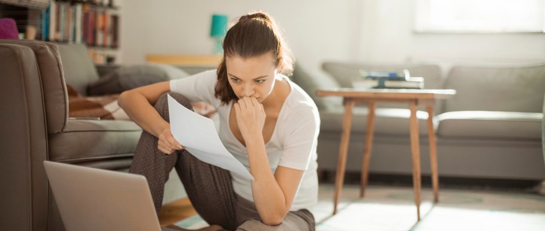 Woman sitting on floor while looking at papers and laptop.