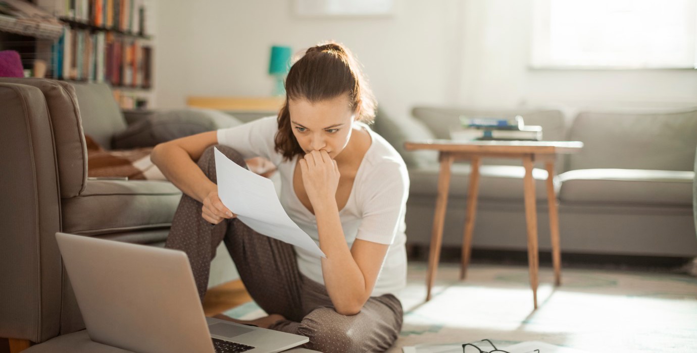 Woman sitting on floor while looking at papers and laptop.