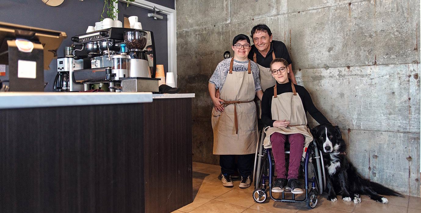 3 workers and a dog smiling in a coffee shop.