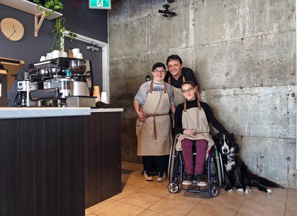 3 workers and a dog smiling in a coffee shop.