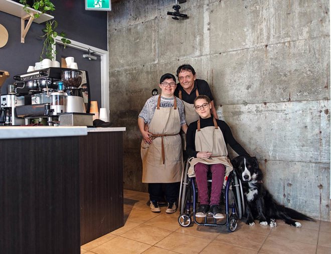 3 workers and a dog smiling in a coffee shop.