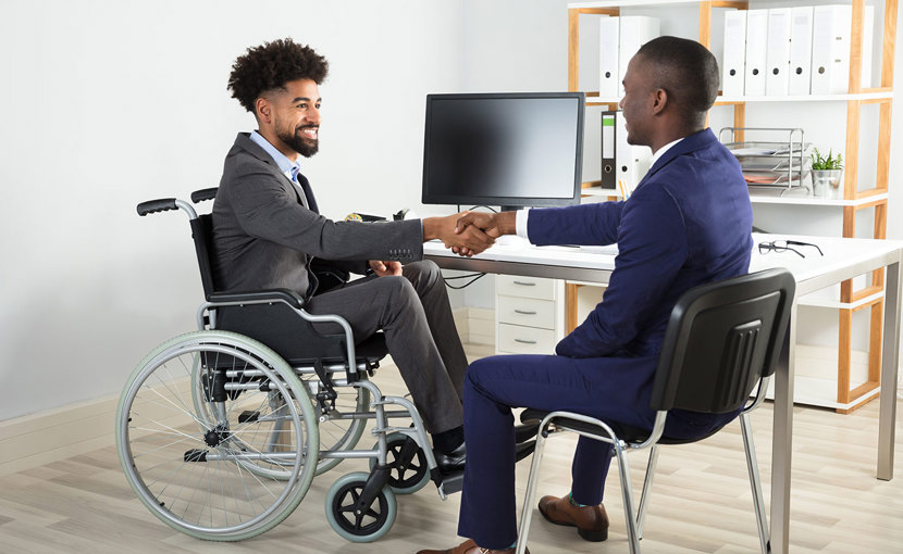 A person in a wheelchair shaking hands with someone in an office.