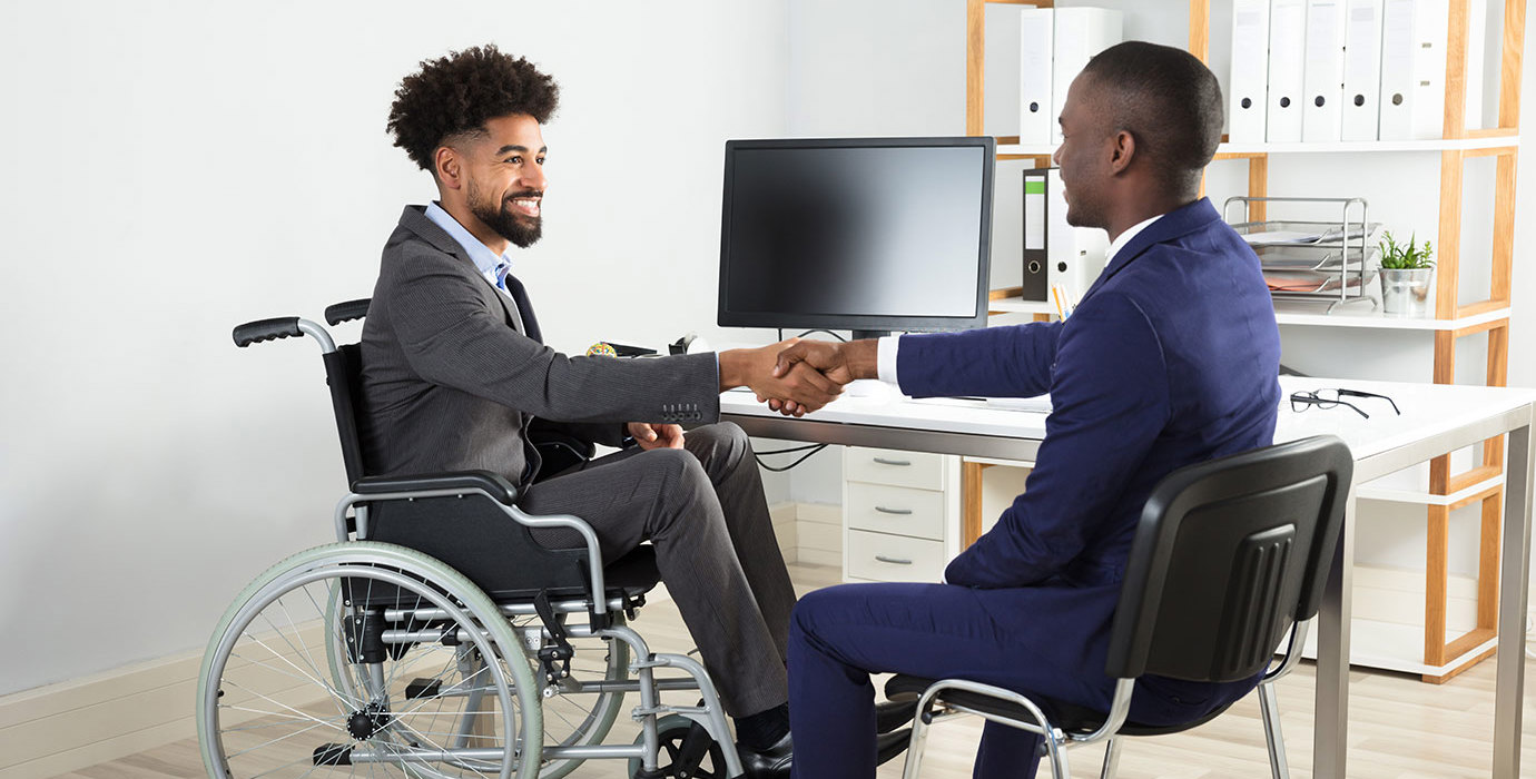 A person in a wheelchair shaking hands with someone in an office.