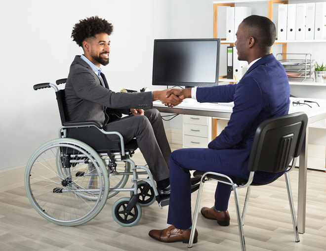 A person in a wheelchair shaking hands with someone in an office.