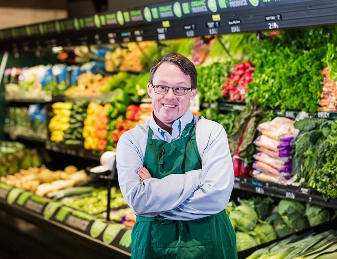 A person smiling in the produce section of a grocery store.